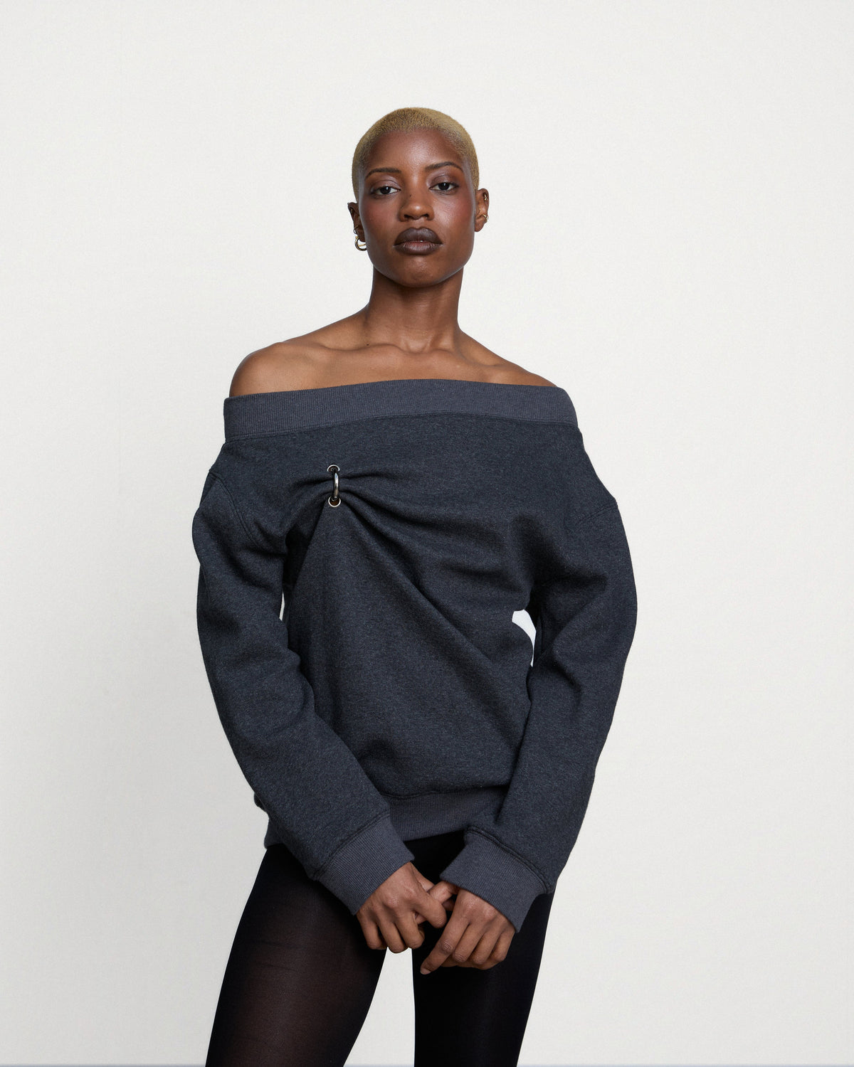 Woman wearing the Stadion Grab sweater in charcoal knit, pulled off one shoulder and gathered by a ring