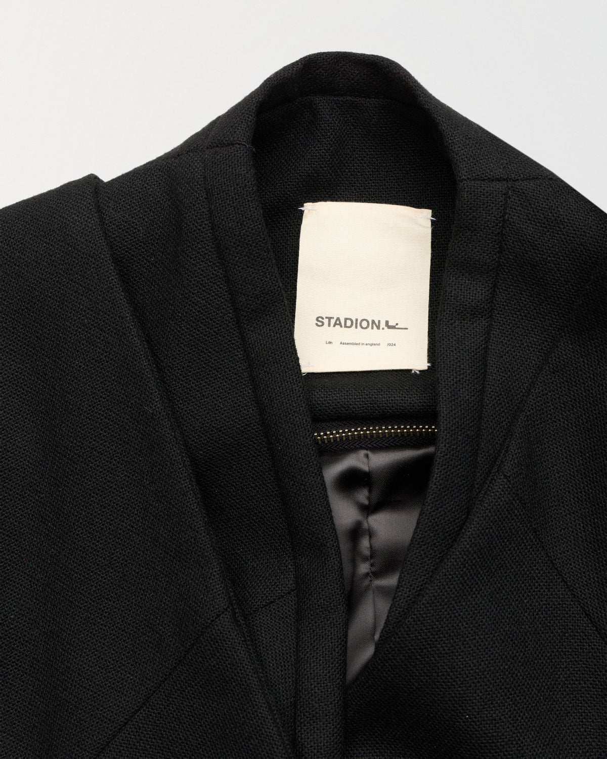 Detail of the collarless neckline, internal zip and woven Stadion label on the Haiden jacket