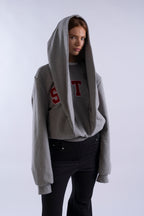 Side angle of model wearing grey STN Collegiate Hoodie by Stadion, featuring oversized hood and red collegiate S T lettering.”
