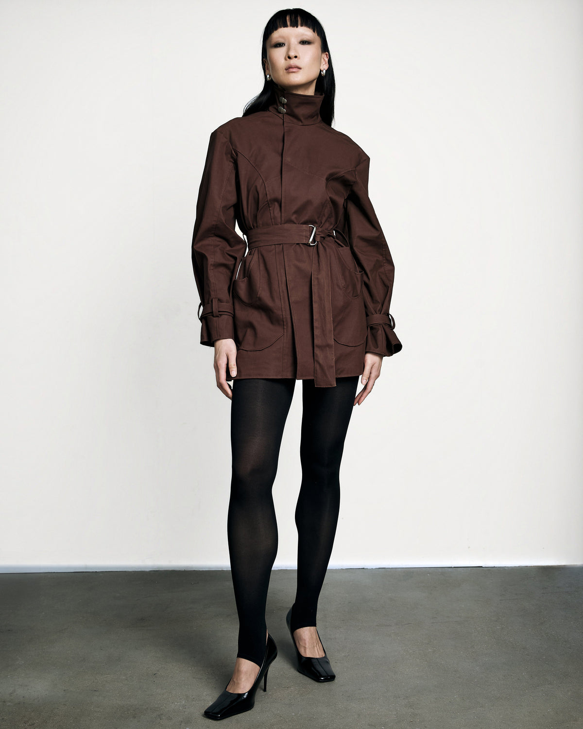 Woman wearing the Stadion Sylvia trench dress in brown with black tights and heels
